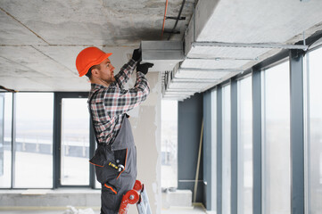 Construction worker installing ventilation system in building