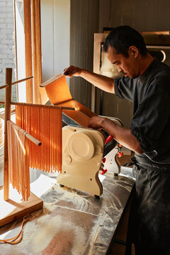 Vertical medium long shot of modern restaurant chef preparing for workday cutting pasta dough using machine in morning