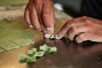 Horizontal close-up shot of unrecognizable chef hands making farfalle pasta out of green dough