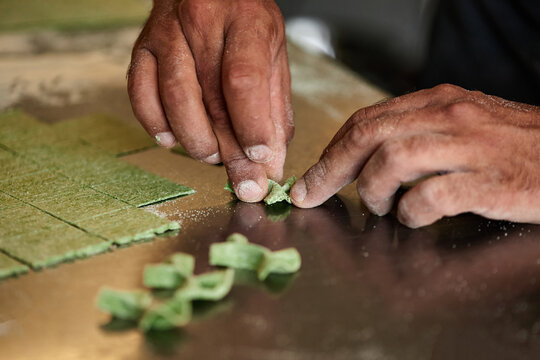 Horizontal close-up shot of unrecognizable chef hands making farfalle pasta out of green dough
