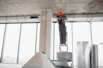 Construction worker installing ventilation system on a ladder in building under construction