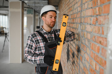 Construction worker using spirit level on brick wall during renovation