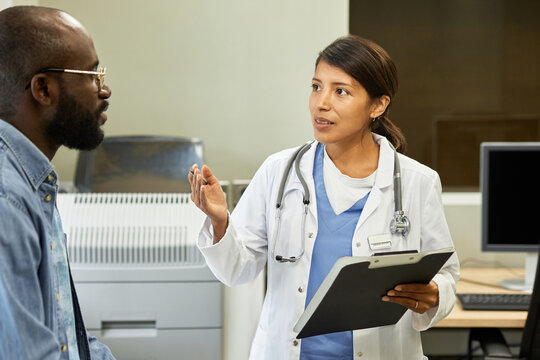 Portrait of beautiful Hispanic woman working as general practitioner in modern hospital consulting her African American patient