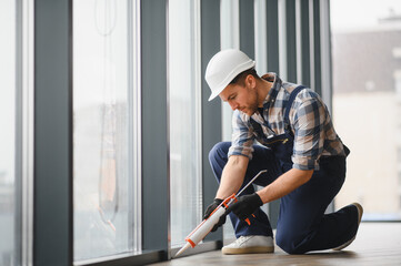 Construction worker sealing window frame with silicone gun in modern building