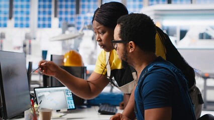 Black engineers collaborate on photovoltaic system designs at computer, focused on eco friendly...