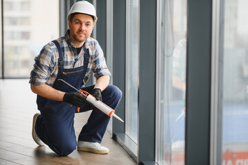 Construction worker applying sealant to window in modern building