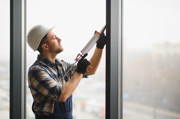 Construction worker sealing window frame with silicone gun in modern building