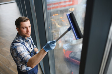 Window cleaner cleaning glass facade using squeegee in modern building