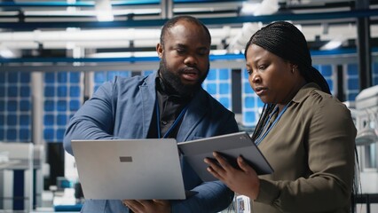 African american engineers team collaborating in a solar panel facility, examining blueprints to...