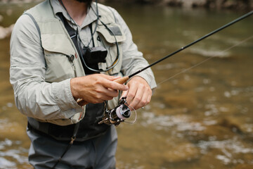 Fisherman reeling fishing line while trout fishing in river