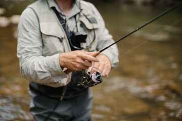 Fisherman reeling line while trout fishing in river