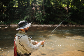 Fisherman casting line in river, trout fishing in mountain stream