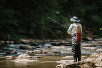 Fisherman casting line in pristine river, engaging in trout fishing