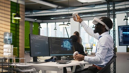 Programmer wearing VR headset at office desk developing programs using AI automation. Startup...