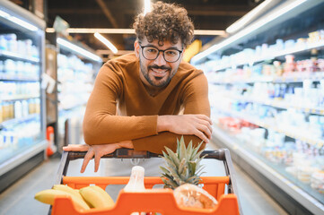 Smiling arab man leaning on shopping cart in supermarket