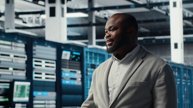 Smiling employee walking in high tech data center with machines powering networks, running companies databases. Admin overseeing server farm with rigs modules processing large datasets, camera B