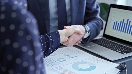 Two business people professionals shaking hands in office setting, sealing a deal with laptop and...