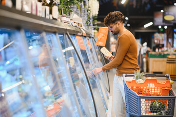 Man choosing frozen food in supermarket refrigerator section