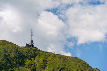 towering communication antenna perched atop a green Swiss mountain, surrounded by stunning clouds...