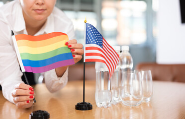 Closeup of rainbow flag and national flag of United States in hands of female office manager...