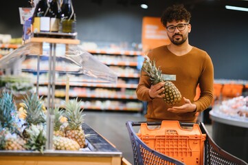 Arab customer choosing pineapple in supermarket holding shopping cart