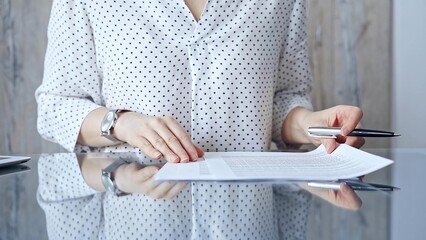 Businesswoman is signing corporate contract at her office desk in formal white blouse with polka...