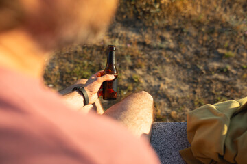 Closeup of a young man, that drinks beer from a bottle, while enjoying the sunset ligth, in...