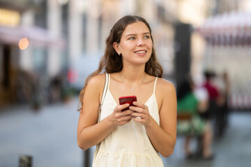 Happy young woman with mobile phone in her hands walking around the city and taking pictures of...