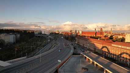 Urban aerial view at sunset showing busy roads, modern traffic infrastructure, and a historic European skyline under golden light.
