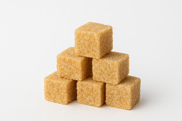 Stack of brown sugar cubes arranged in a pyramid shape on a white background. concept of sweetener, baking ingredient, kitchen stock.