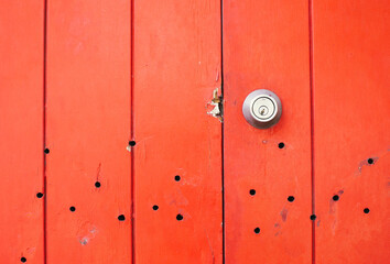 Vivid red wood panels with signs of age are punctuated by small holes and a scratched surface. A...