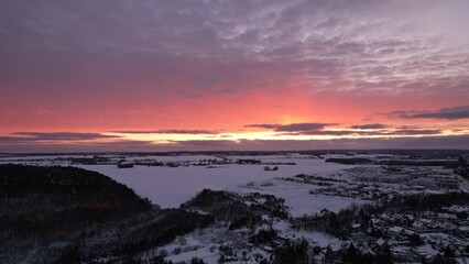 Panoramic view of a snow-covered landscape and frozen lake under a vivid winter sunset with dramatic purple and orange clouds.