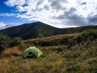 Green camping tent on mountain slope with scenic peaks in the background. Outdoor adventure, hiking and wild camping in the mountains.