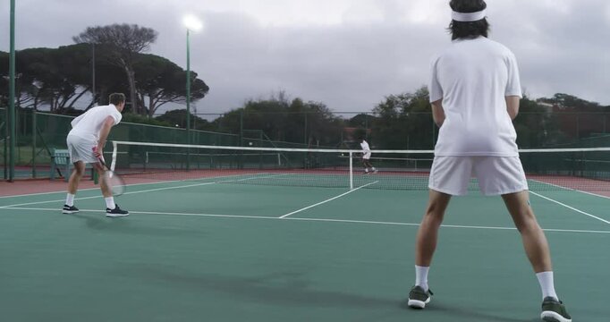 After server tossing ball, male tennis partners volleying then lobbing point-winning shot on court