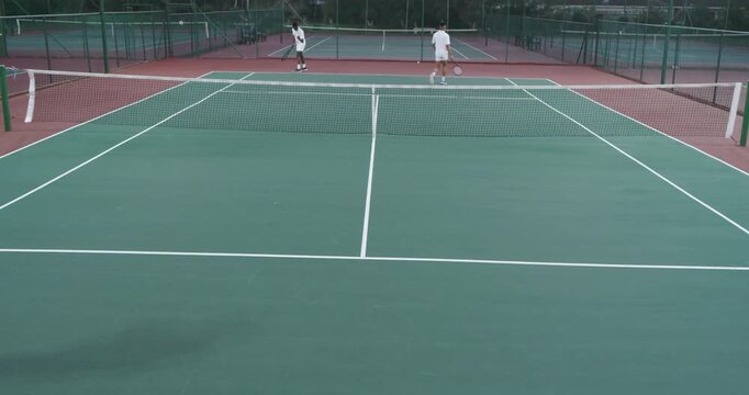 Serving diverse male tennis partners sparking fast volley rally at outdoor club, with rackets, ball