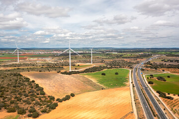 Wide aerial view of wind turbines on open fields next to highway. Renewable energy infrastructure...