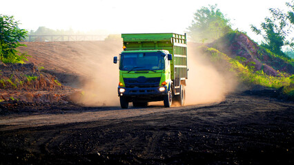 Green mining dump truck kicking up dust on a rugged mining road, transporting heavy material across the construction site © Aryanto