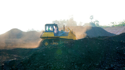 Massive yellow mining bulldozer working on a coal mine, moving large amounts of earth with dust in the air