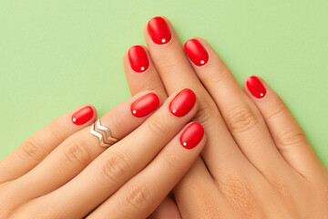 Close up womans hands with red minimalist nail design on green background