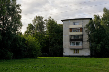 Isolated concrete apartment block with weathered facade and empty balconies, surrounded by wild...