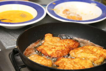 Fried breaded chicken fillets cooking in hot oil on black pan. Homemade schnitzel preparation with...