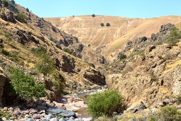 Narrow mountain stream flowing between steep rocky cliffs in Boshkyzylsay, Uzbekistan