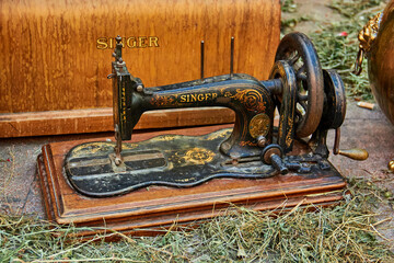 An antique Singer sewing machine with ornate details is displayed on a wooden base, showcasing craftsmanship during the Crosses of May in Granada. Vintage, tradition.