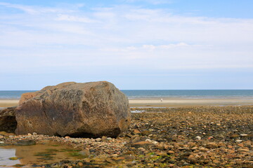 Colorful boulder and rocks exposed at low tide serve as a barrier to soft sand and ocean waves