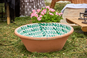 A large terracotta bowl with a green zigzag interior pattern holds pink geranium flowers, set...
