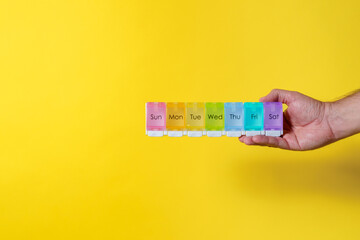 7 day weekly pill organizer male hand on yellow background with copy space