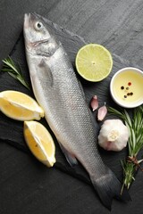 Fresh raw seabass with spices on black table, top view. Fish and seafood delicacies
