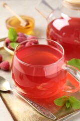 Tasty raspberry tea in glass cup, teapot, berries, honey and mint on table, closeup