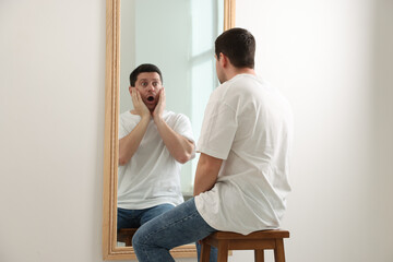 Man looking at shocked reflection of himself in mirror indoors. Mental health