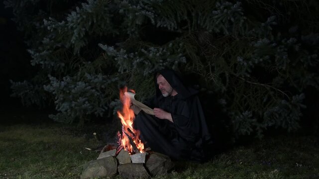 a sorcerer in a black robe reads spells from a mys
